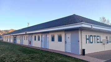 A hotel with a row of rooms numbered 25 to 31, a tiled roof, and a grassy area in front.