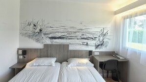 Une chambre d’hôtel moderne avec une grande fresque murale, une tête de lit en bois, deux lits, un bureau et une chaise.