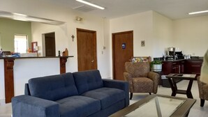 Un salon avec un canapé bleu, un fauteuil à motifs et une table basse. Il y a également un coin cuisine équipé d’un réfrigérateur, d’une cuisinière et de placards.