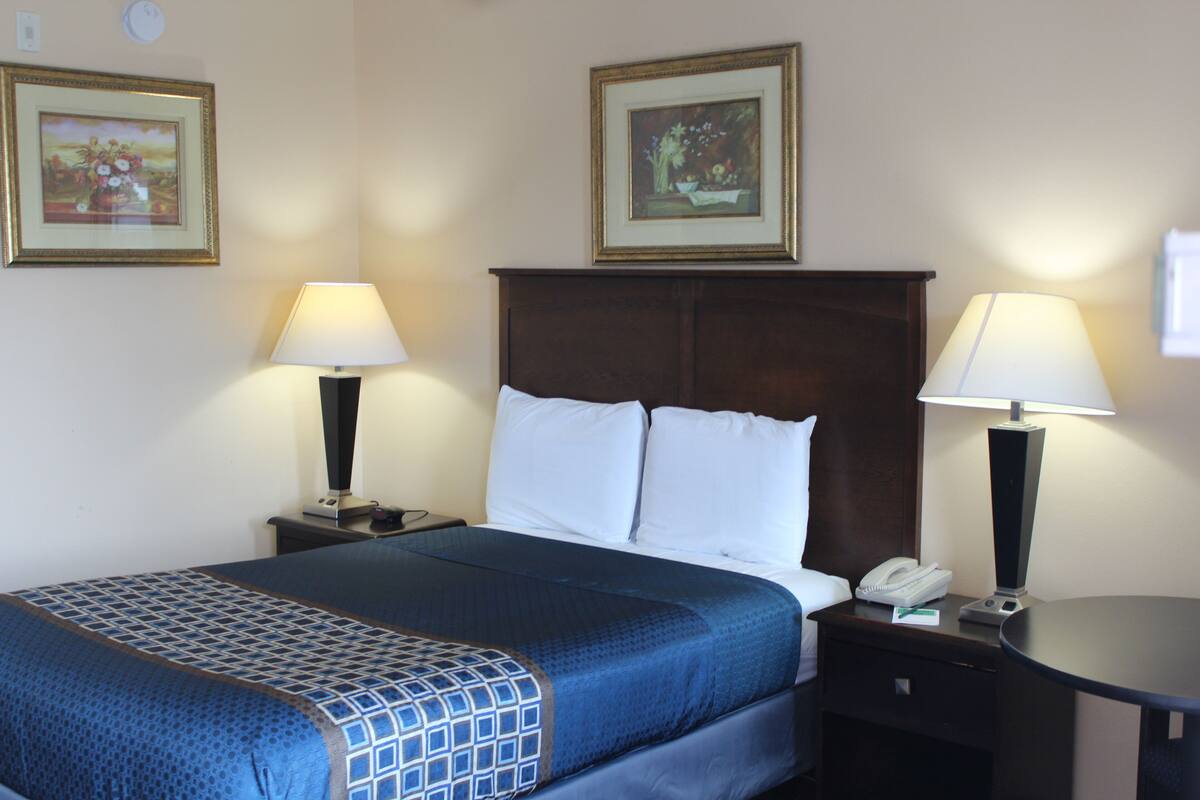 A hotel room with a large bed, two bedside tables with lamps, a nightstand with a phone, and two framed pictures on the wall.