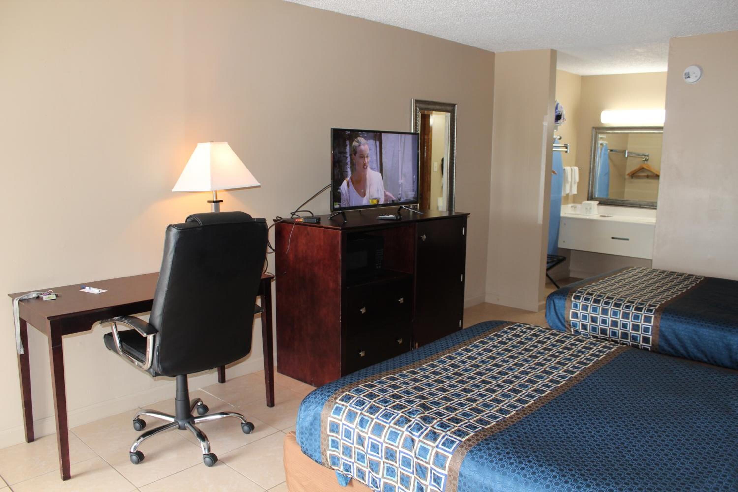 A hotel room with a desk, chair, television, two beds, and a bathroom visible through an open door.