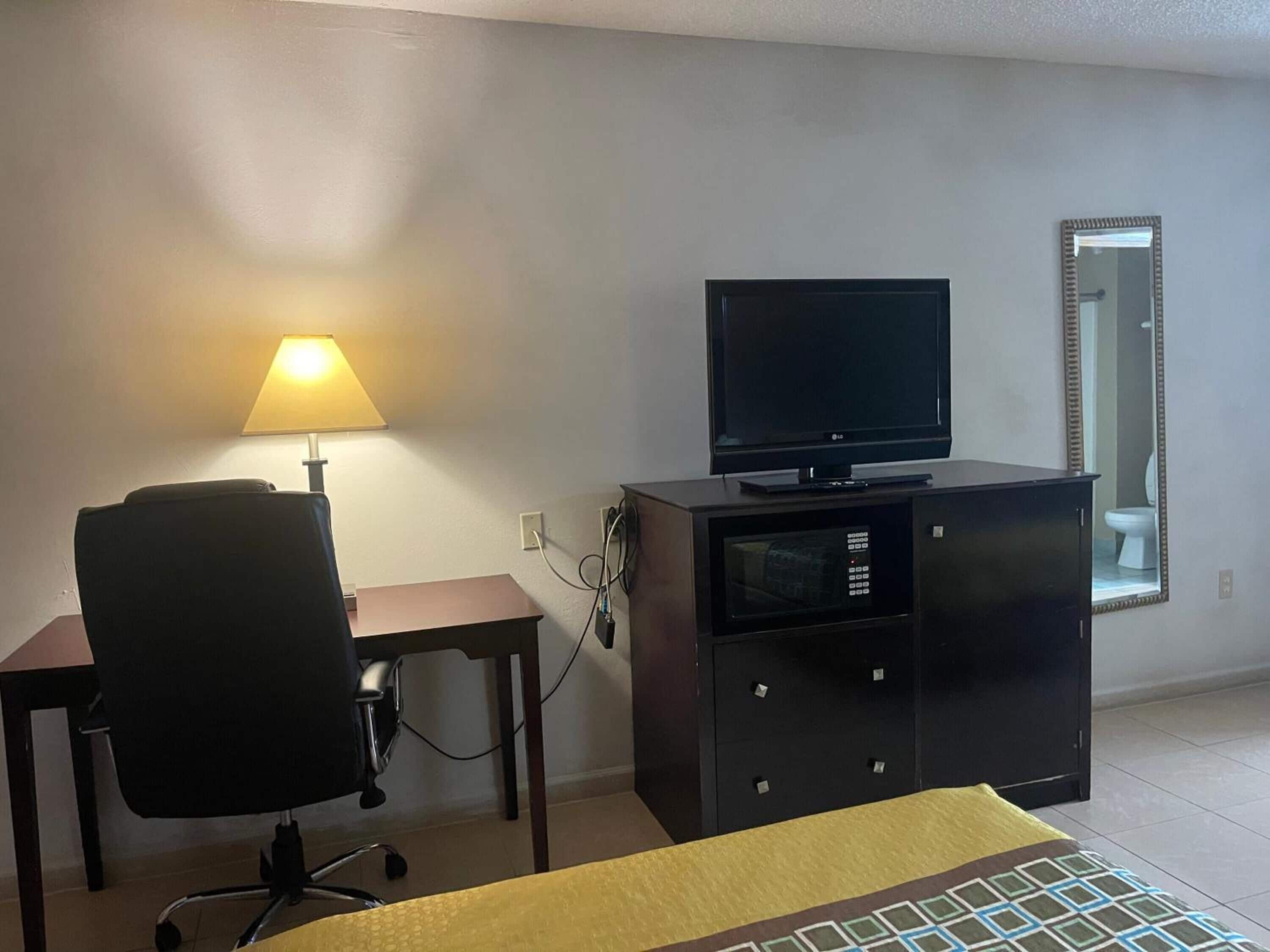 A small room with a desk, chair, TV, and a mirror.