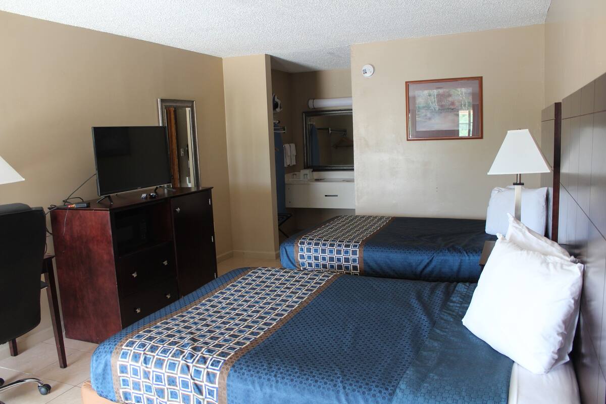 A hotel room with two beds, a desk, a TV, a dresser, and a bathroom visible through an open door.