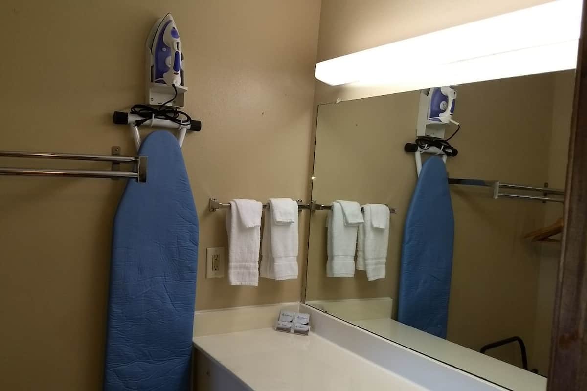 A bathroom with a blue ironing board, a white sink, and a mirror reflecting the ironing board and towels.