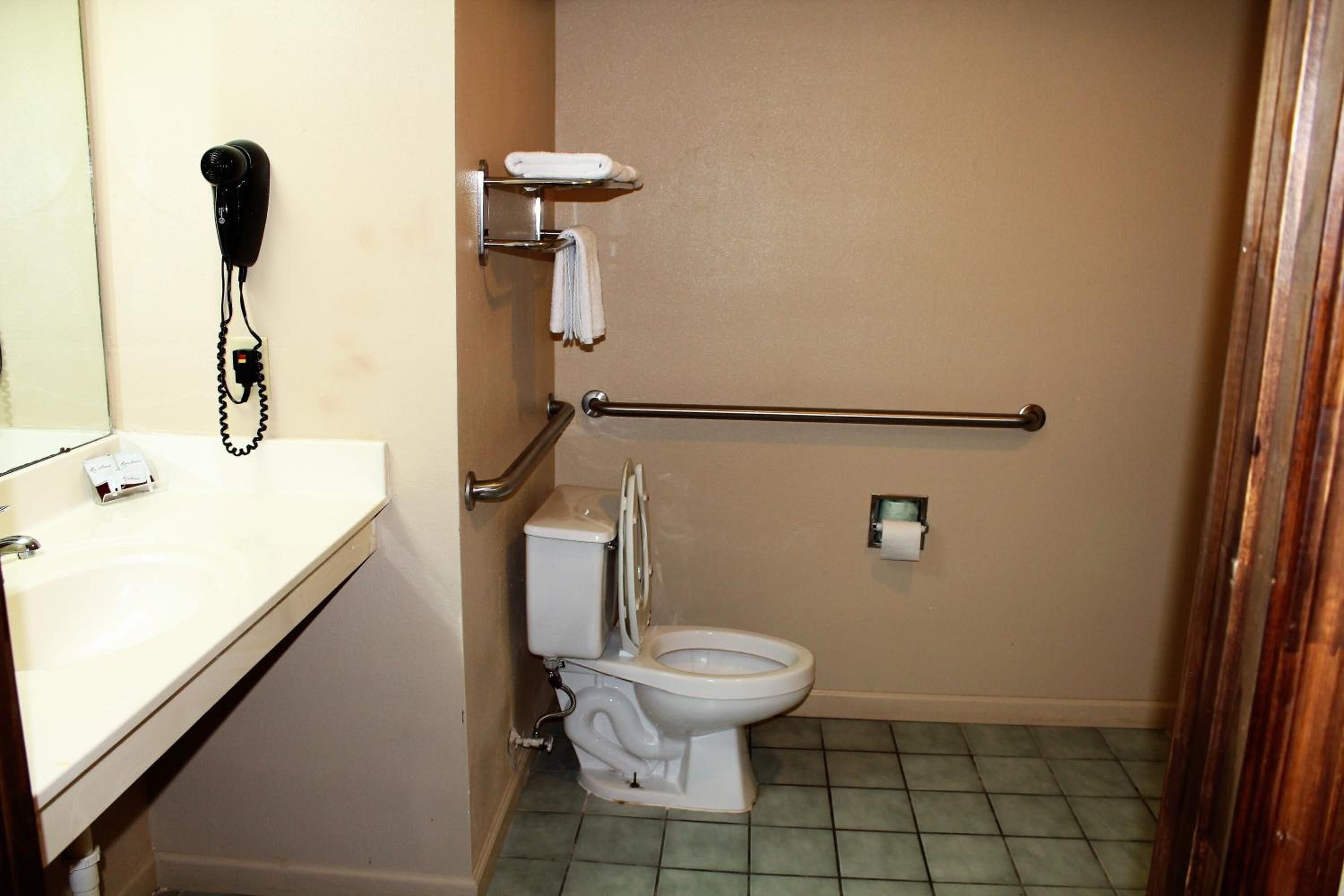 Un baño pequeño con inodoro, secamanos, toallero y dispensador de jabón.