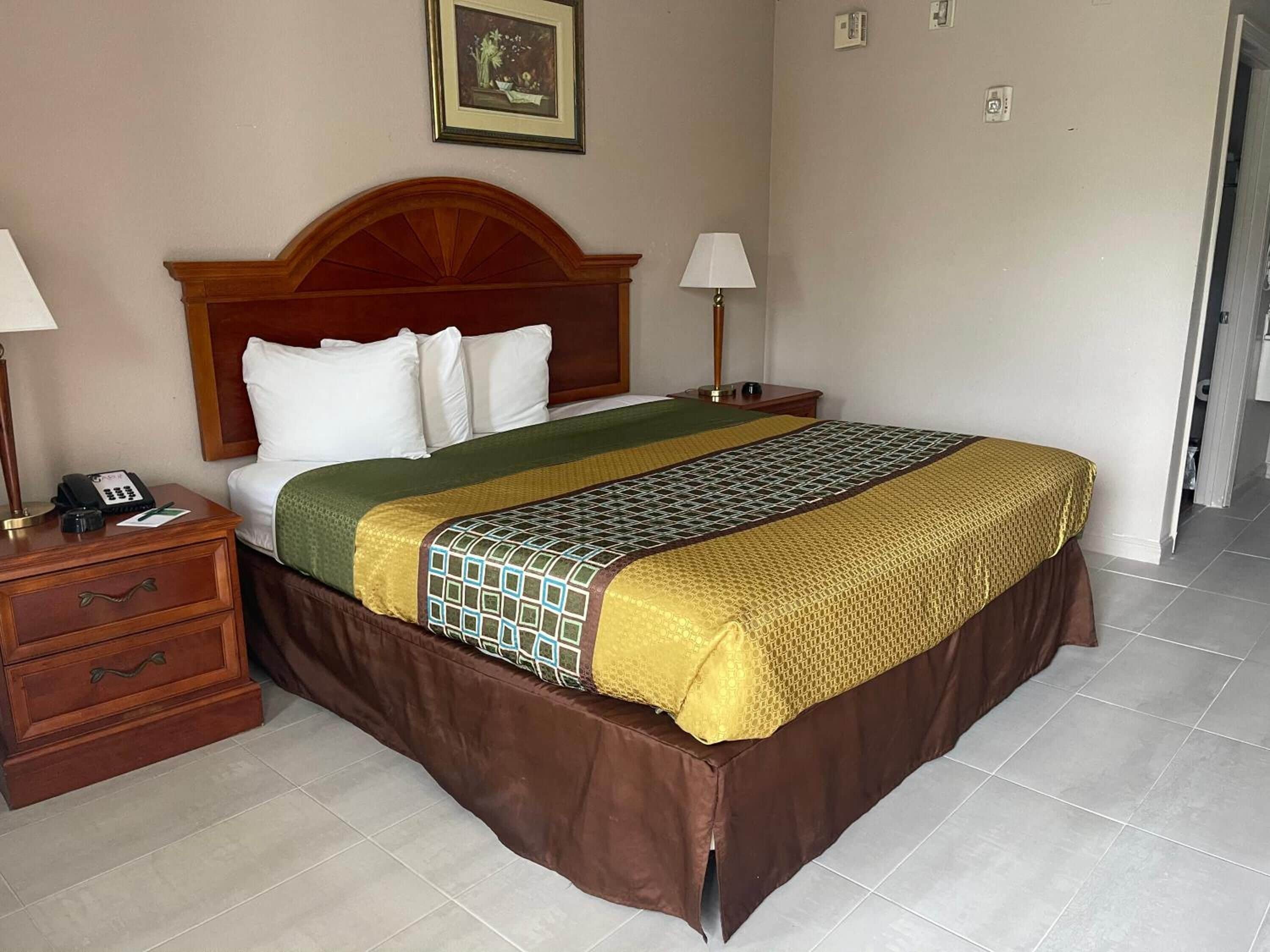 A hotel room with a large bed, wooden headboard, two bedside tables with lamps, a telephone, and a framed picture on the wall.