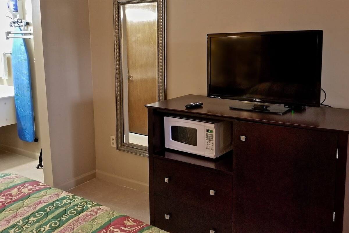 A bedroom with a bed, a television, a microwave, and a dresser.