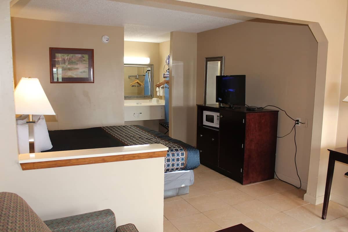 A hotel room with a bed, a desk with a lamp, a television, a microwave, and a bathroom visible in the background.