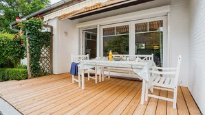 A wooden deck with a table and chairs, a bottle of orange juice, and a bowl of fruit. - House 7 "Beach Pirate" (ID 023) (Room category) - House 7 "Beach Pirate" (ID 023) (Sankt Peter-Ording)