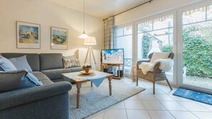 A living room with a sofa, a coffee table, a television, and a wicker chair. - House 7 "Beach Pirate" (ID 023) (Room category) - House 7 "Beach Pirate" (ID 023) (Sankt Peter-Ording)