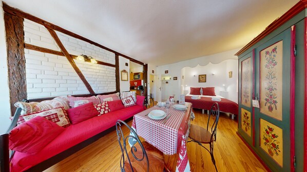 A cozy room with a red sofa, a dining table set with plates, and a bed with red bedding.