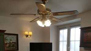 Spiseområde med bord, stole, loftventilator, fjernsyn og et vindue med persienner.