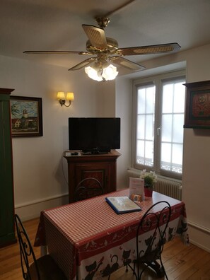A dining area with a table, chairs, a ceiling fan, a television, and a window with blinds.
