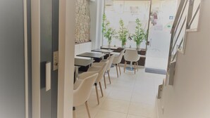Un comedor moderno con mesas y sillas, una pared de acento de piedra y plantas en macetas.