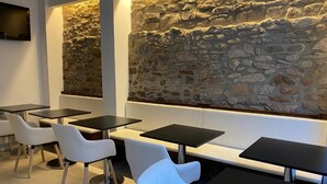 Un interior de restaurante moderno con paredes de piedra, sillas blancas acolchadas y mesas negras.