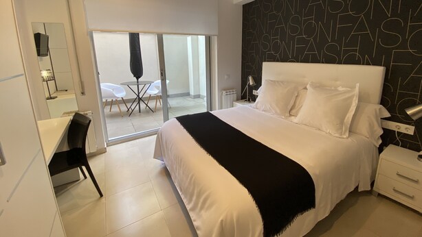 Una habitación de hotel moderna con una cama grande, un escritorio y una silla. Cuenta con un balcón con mesa y sillas.