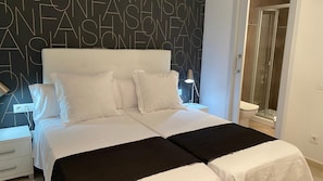 A double bed with white bedding and black throw pillows, a bedside table, and a wall with a geometric pattern. - Hostal Somnis (Suria)