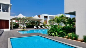 A modern hotel with a swimming pool, lounge chairs, and a covered patio area. - Four Points by Sheraton Mahabalipuram Resort & Convention Center (Tirukalukundram)