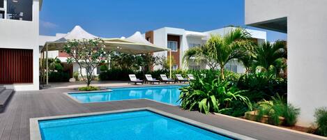 Un hotel moderno con piscina, sillas de descanso y un patio cubierto.
