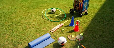 A grassy field with sports equipment including a soccer ball, hula hoop, badminton racket, and a ball of croquet.
