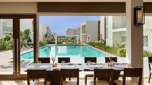A dining area with a view of a swimming pool and surrounding buildings. - Four Points by Sheraton Mahabalipuram Resort & Convention Center (Tirukalukundram)
