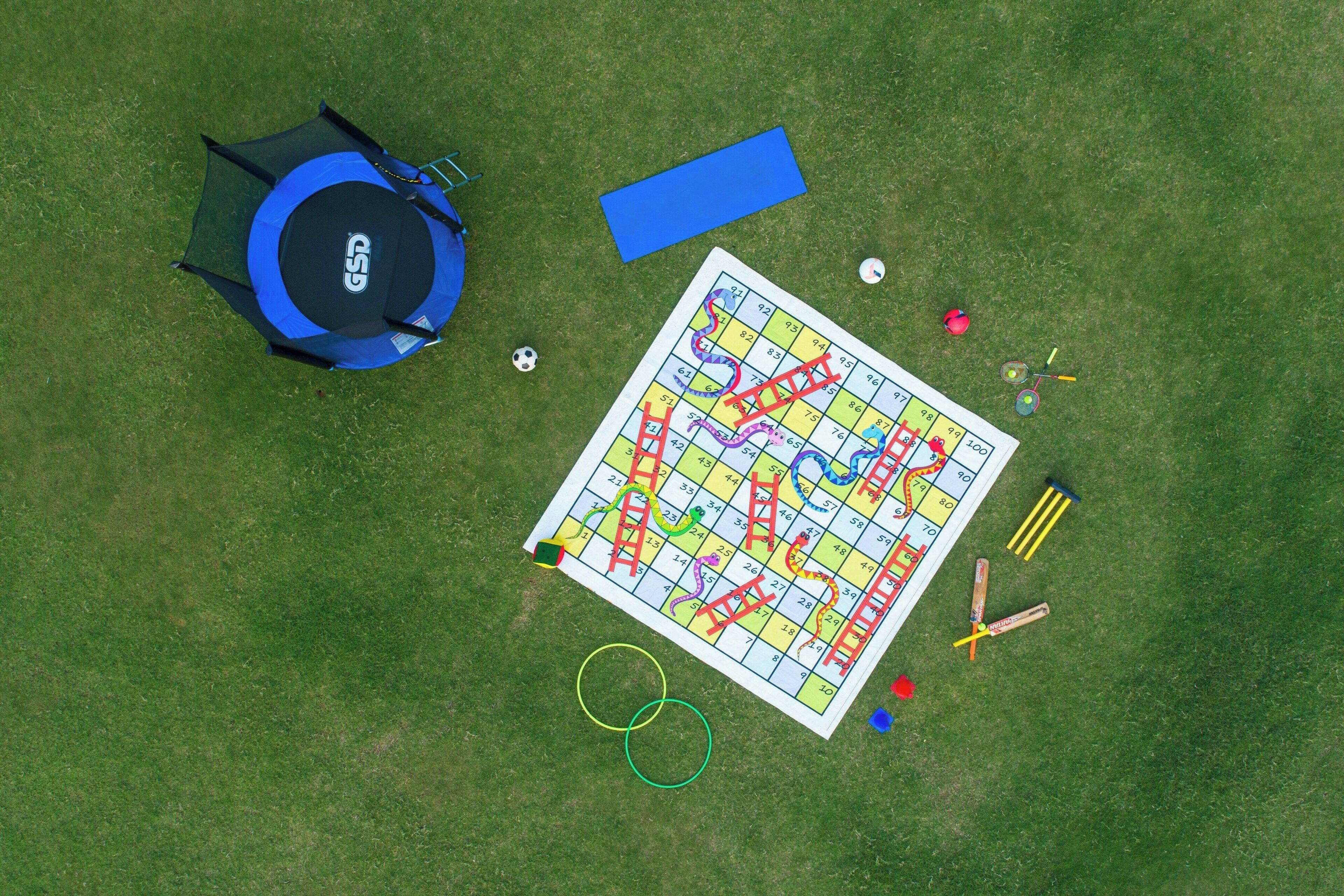 A top-down view of a grassy area with a large, colorful board game, a blue mat, and various game pieces.