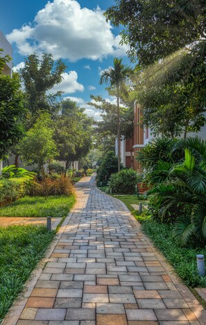 Um caminho pavimentado ladeado por vegetação exuberante e edifícios com fachadas vermelhas e brancas.