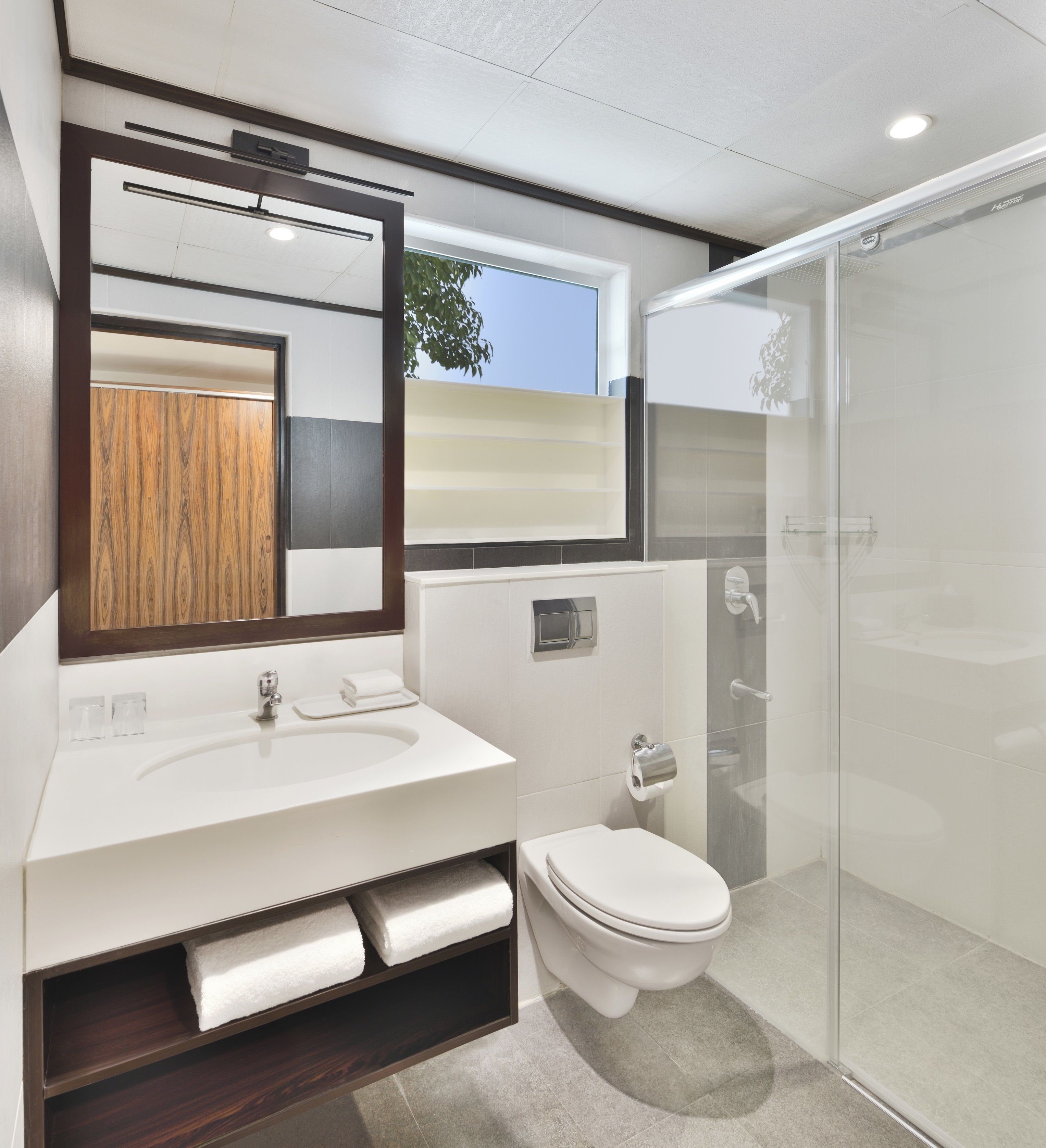 A modern bathroom with a large mirror, white sink, and a glass-enclosed shower.