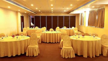 Un salón de conferencias con varias mesas redondas, cada una con sillas y preparación para banquetear.