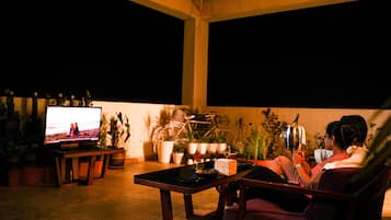 Un área de estar al aire libre acogedora con televisor, plantas en macetas y una mesa.