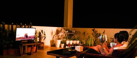 A cozy outdoor seating area with a television, potted plants, and a table.