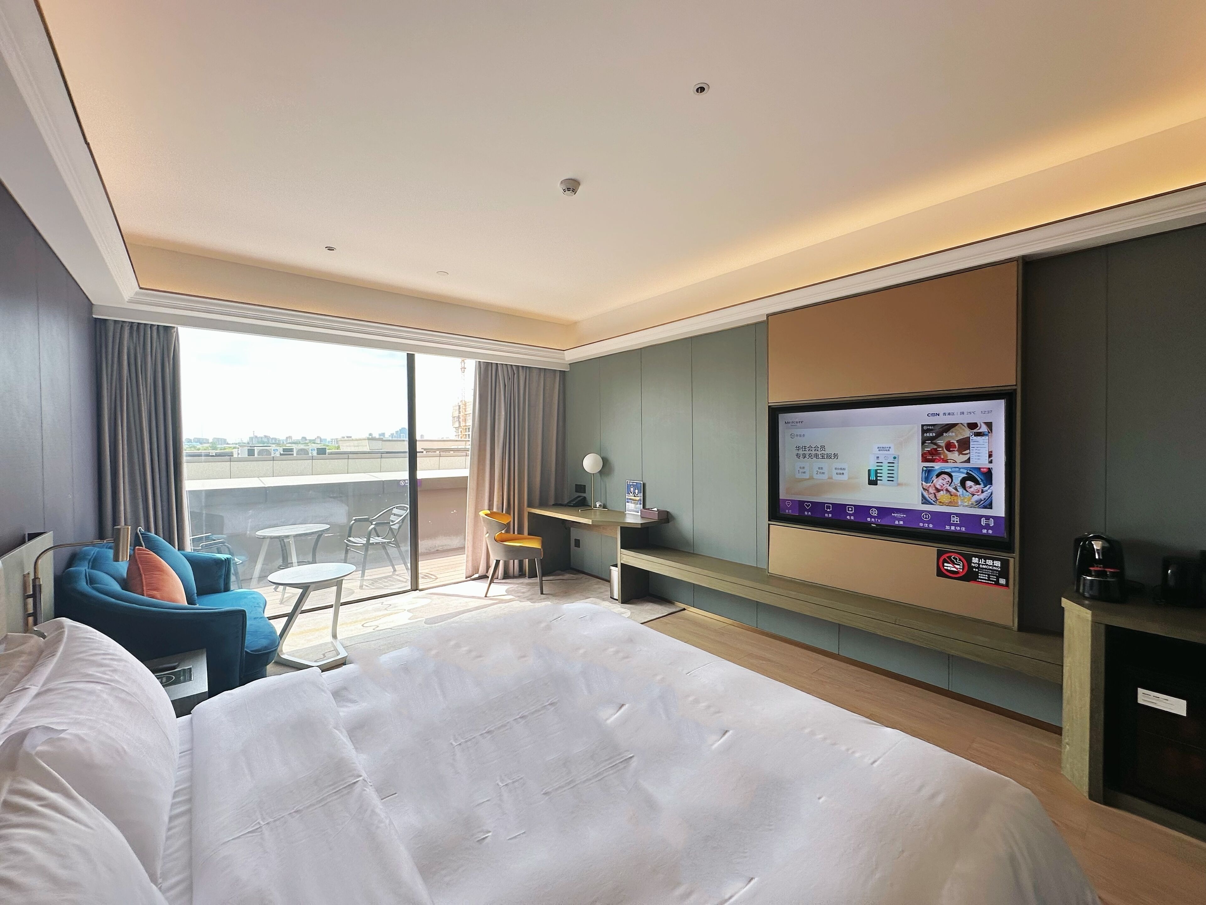 Een hotelkamer met een bed, een bureau, een televisie, een balkon met uitzicht en een zithoek met stoelen.