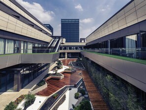 Un edificio moderno con un patio central, barandillas de vidrio y vistas a un rascacielos alto al fondo.