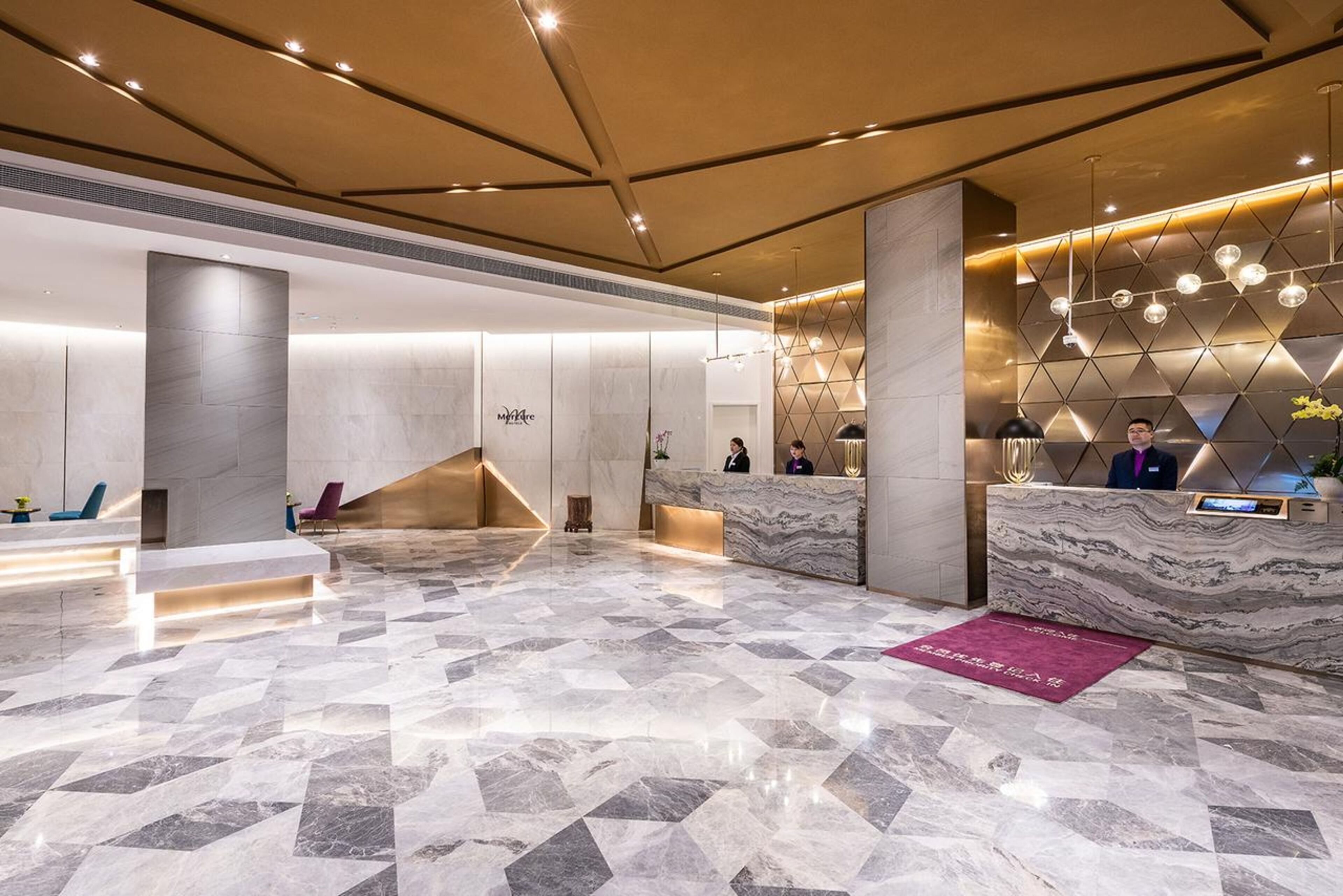 A modern hotel lobby with a marble floor, a reception desk, and a geometric wall design.