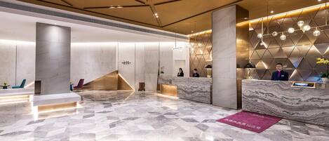 A modern hotel lobby with a marble floor, a reception desk, and a geometric wall design.