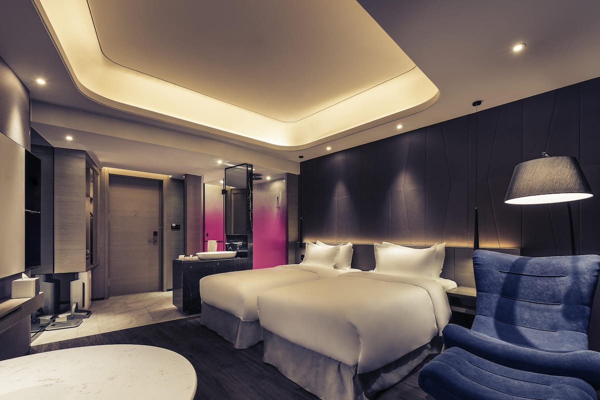 Una habitació d'hotel moderna amb un llit, una taula de nit i un butac armchair blau.