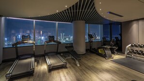Een sportschool met loopbanden, een bank en een halterrek, met stadszicht door grote ramen.
