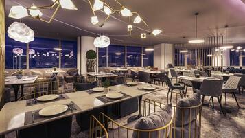 A modern restaurant with multiple dining tables, comfortable seating, and contemporary lighting fixtures.