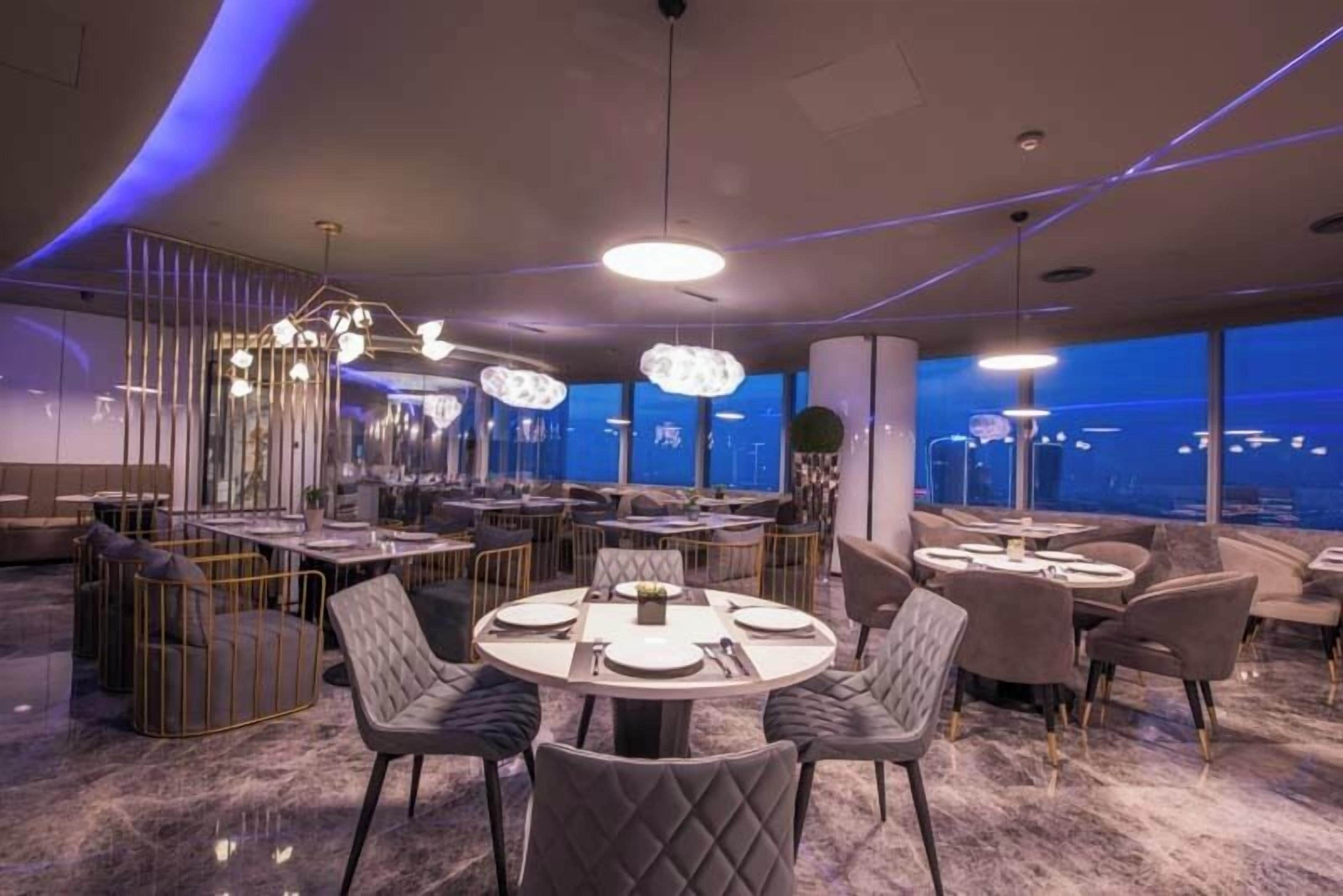 A modern restaurant with round tables, cushioned chairs, and pendant lighting.
