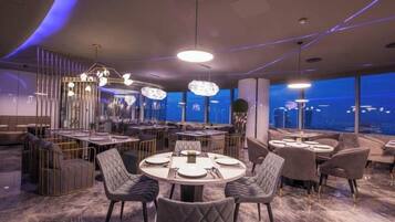 A modern restaurant with round tables, cushioned chairs, and pendant lighting.