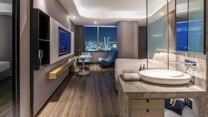 Een moderne hotelkamer met een groot bed, een rond badkamermeubel, een televisie, een bureau en uitzicht op de stad.