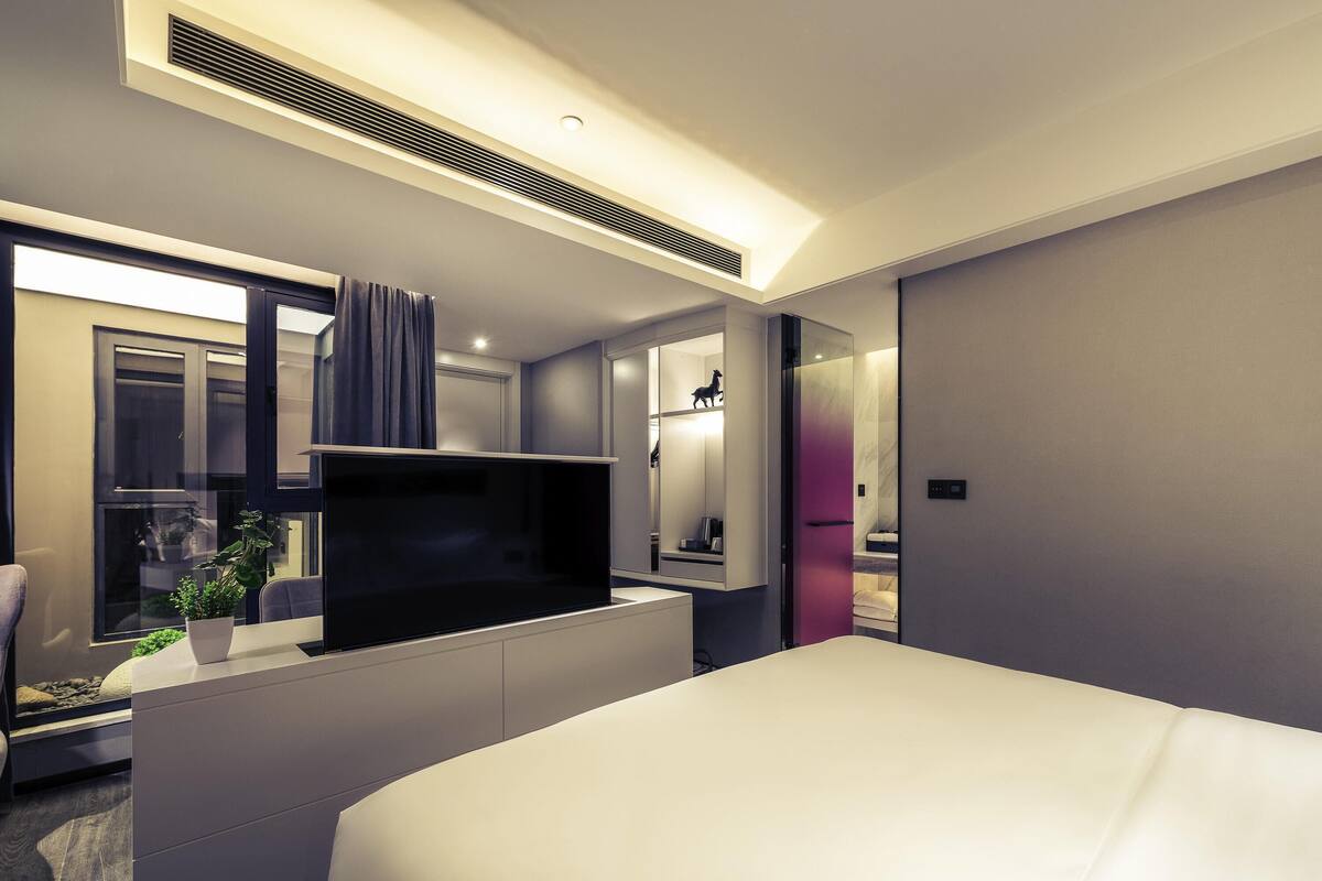 Habitació d'hotel moderna amb llit, televisió de pantalla plana, escriptori i bany visible a través d'una separació de vidre.