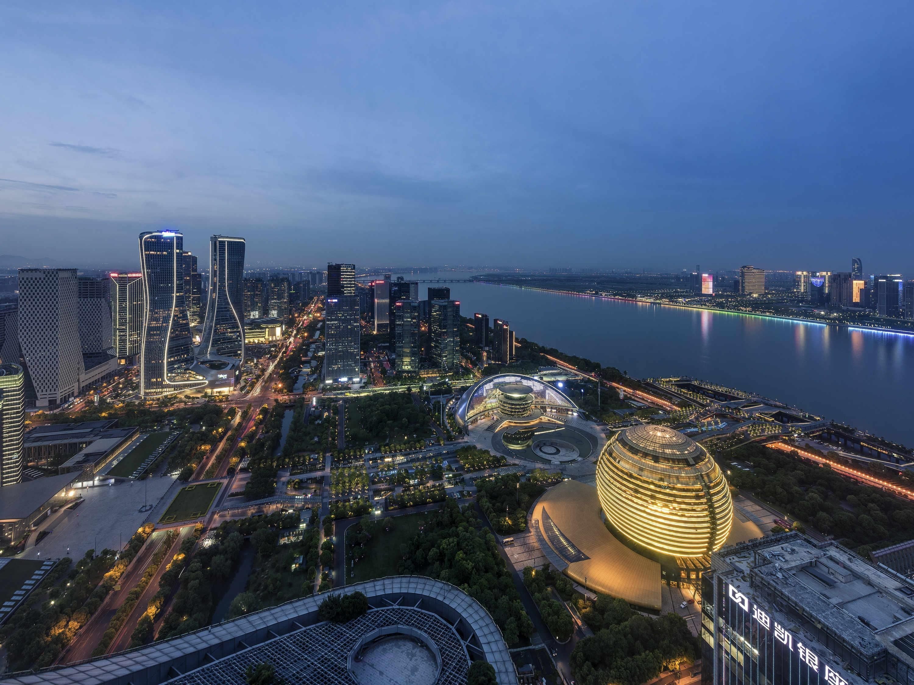 A cityscape with modern buildings, a river, and a round building with a dome.