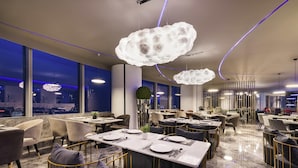 Een modern restaurantinterieur met marmeren vloeren, gouden stoelen en grote ramen met uitzicht op de stad.