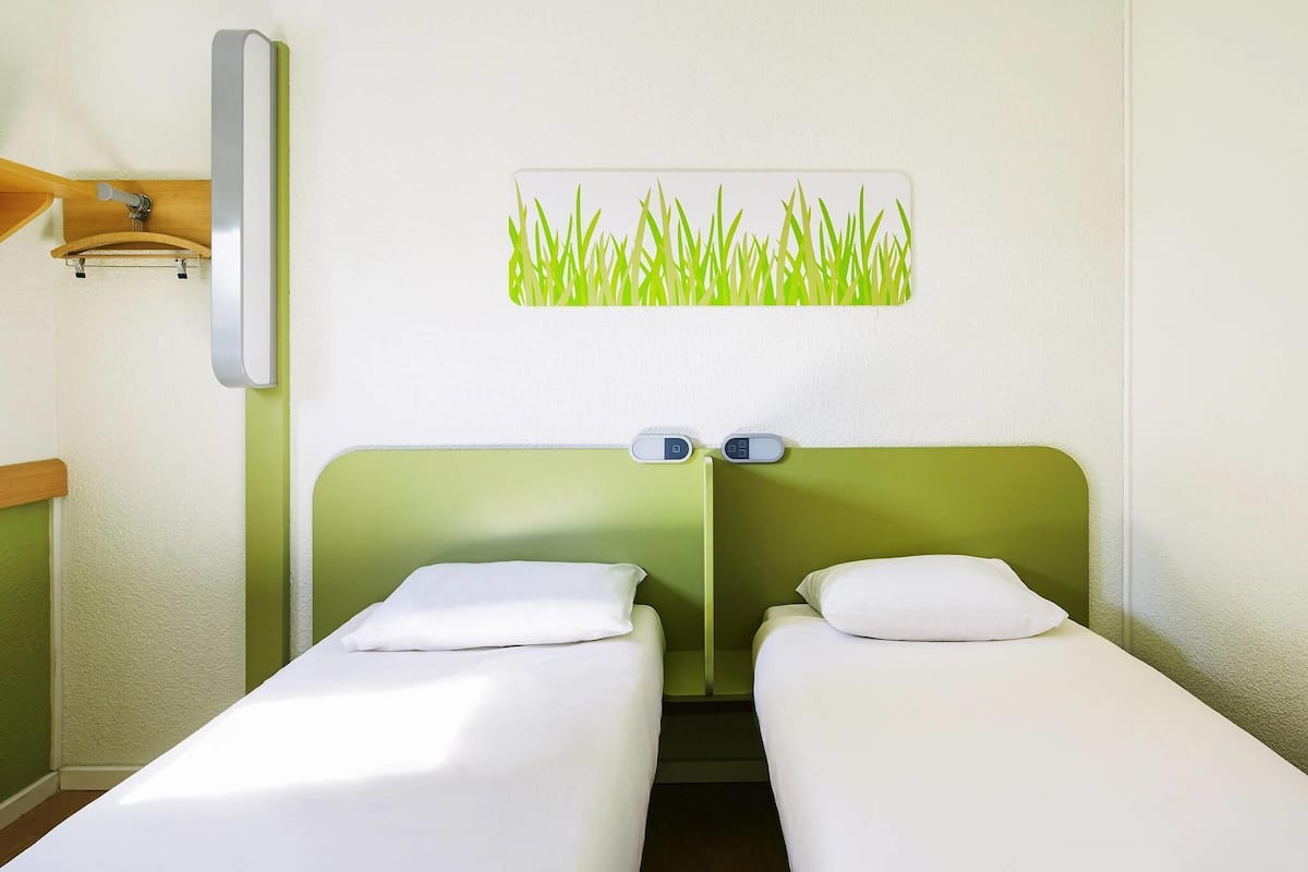 Habitación de hotel con dos camas individuales, una lámpara fijada a la pared y un adorno de hierba en la pared.