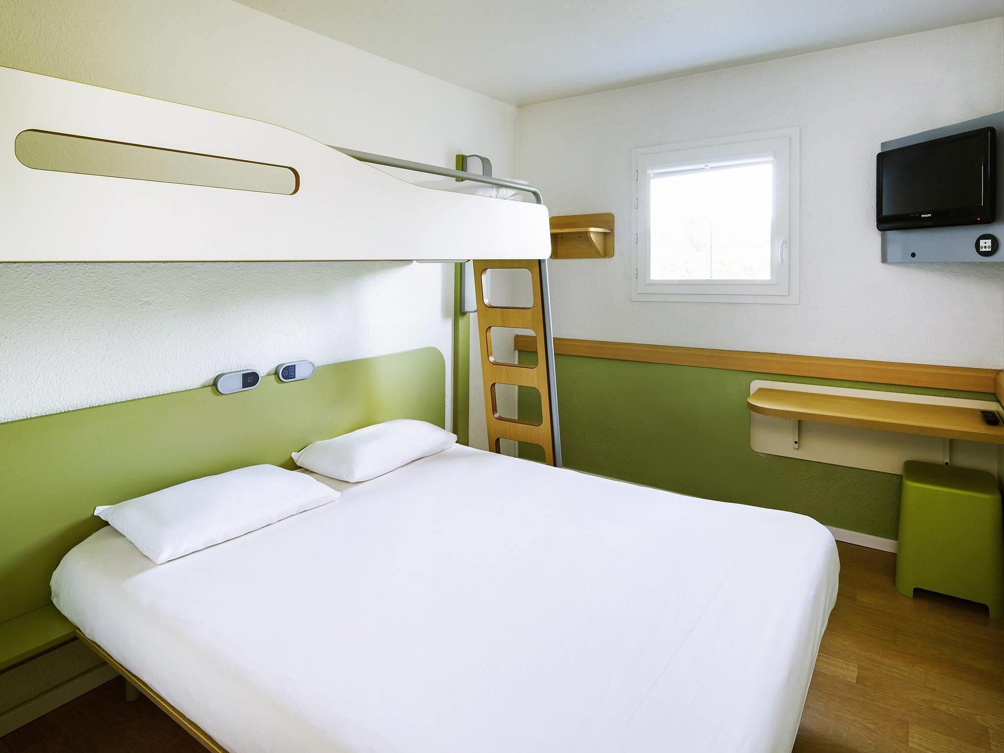 Una cama en literas con una escalera, una mesita de noche, un televisor montado en la pared y una ventana.