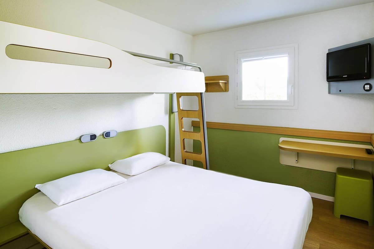Una cama en literas con una escalera, una mesita de noche, un televisor montado en la pared y una ventana.