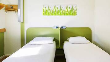 Ein Hotelzimmer mit zwei Einzelbetten, einem grünen Kopfteil, einer Wandlampe und einem Wandbild mit Gras.