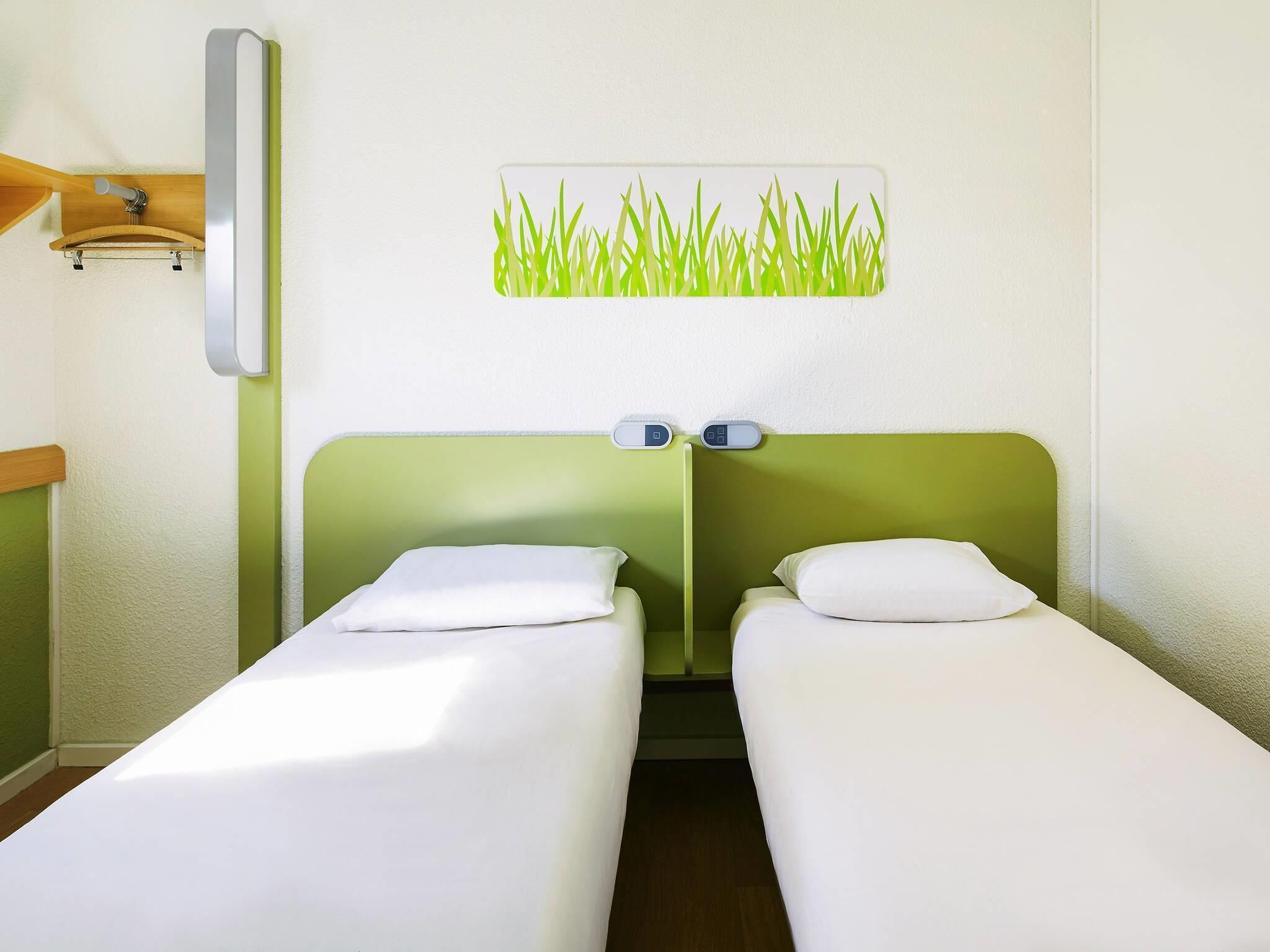 Habitación de hotel con dos camas individuales, una lámpara fijada a la pared y un adorno de hierba en la pared.