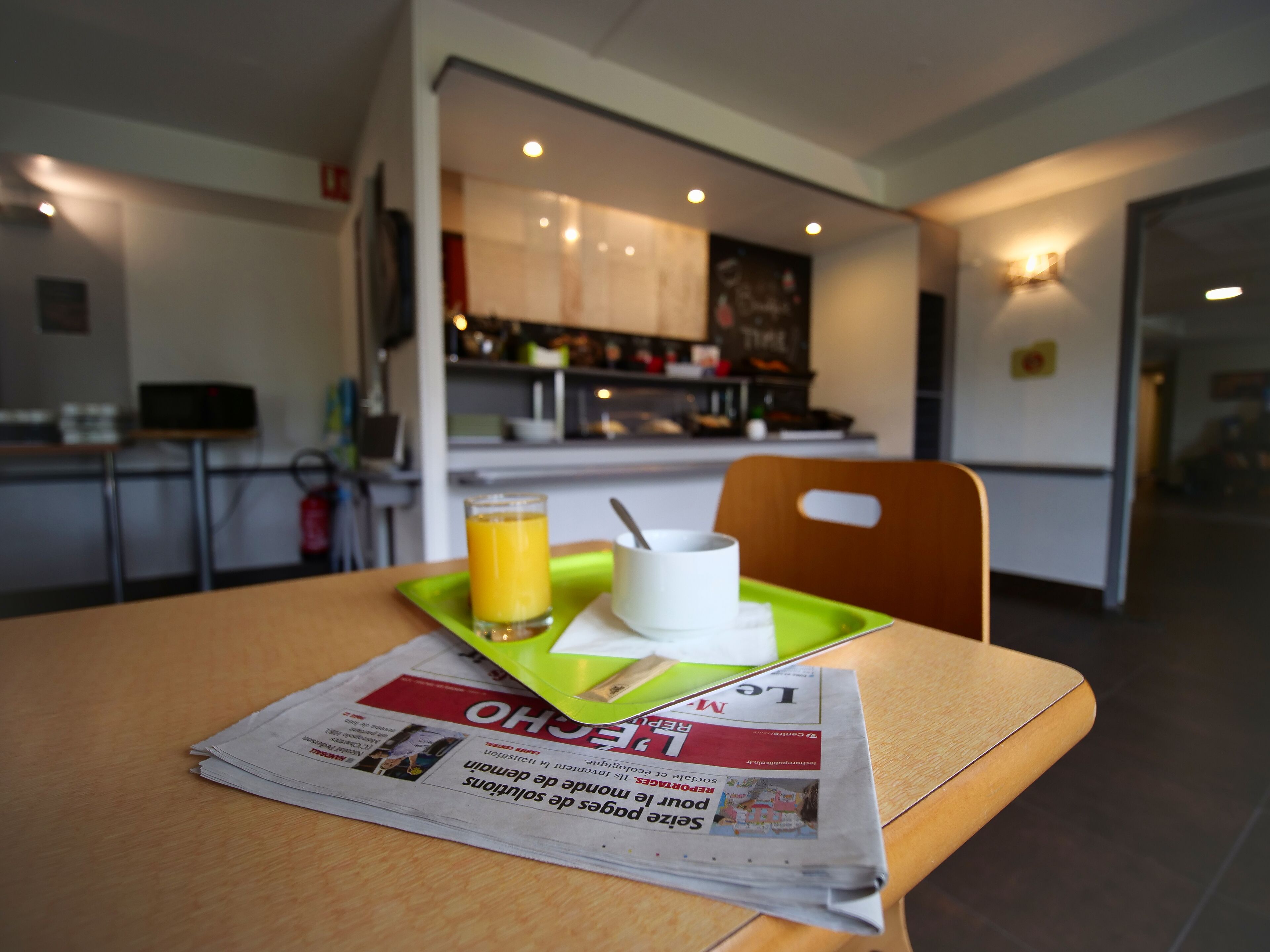 Una presentación de desayuno con un periódico, un vaso de zumo de naranja y una taza blanca sobre una bandeja verde.